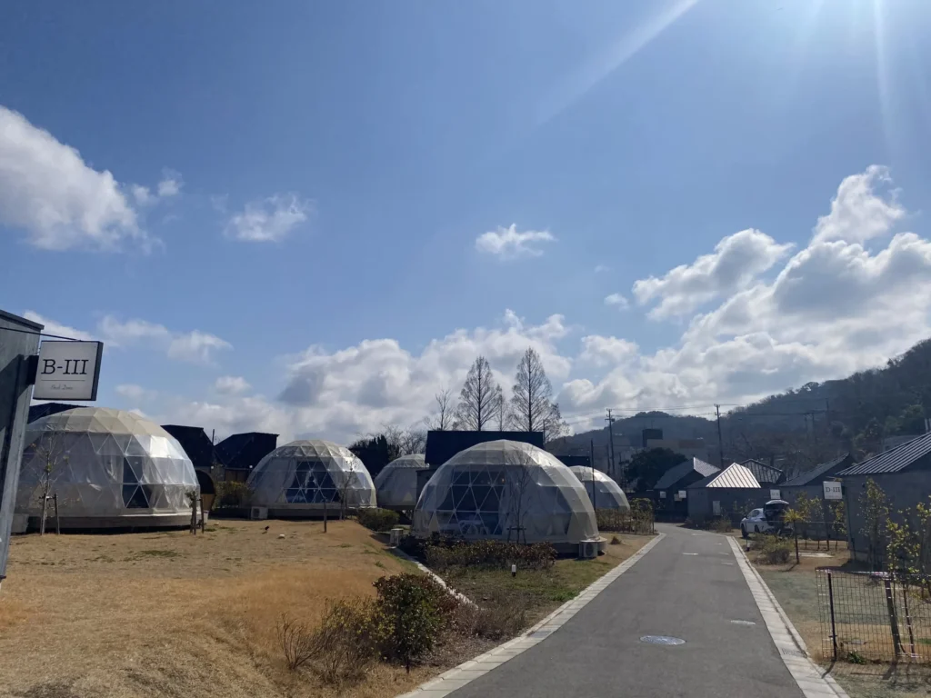 晴れ渡る空の下に陽の光を受けて輝くドームテントがいくつも並ぶ写真