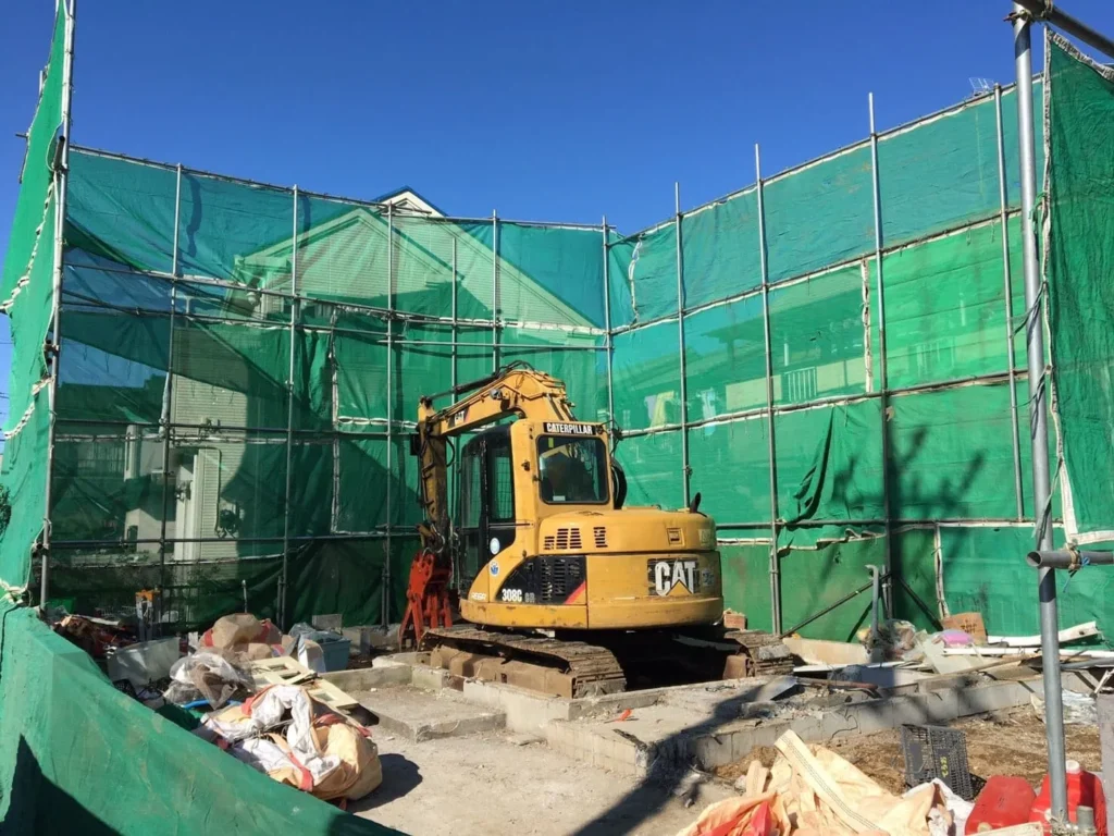 四方を骨組みに囲まれた土地をショベルカーが鳴らしている建築中の画像