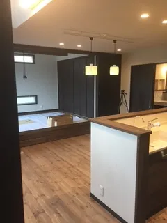 床はナチュラルウッドのフローリングで手前にはアイランドキッチンがあり奥は小上がりの和室になっている20畳ほどのリビング