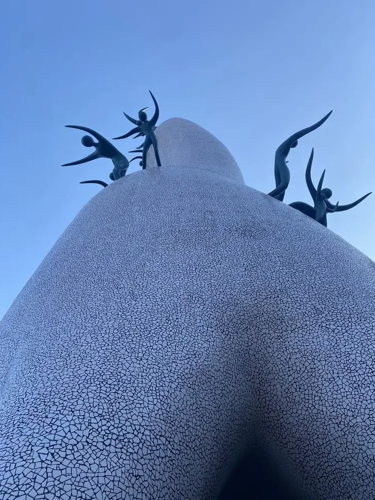 白い塔の上で子供の形の複数のオブジェが生き生きと戯れる巨大な母の塔を真下から見上げた写真